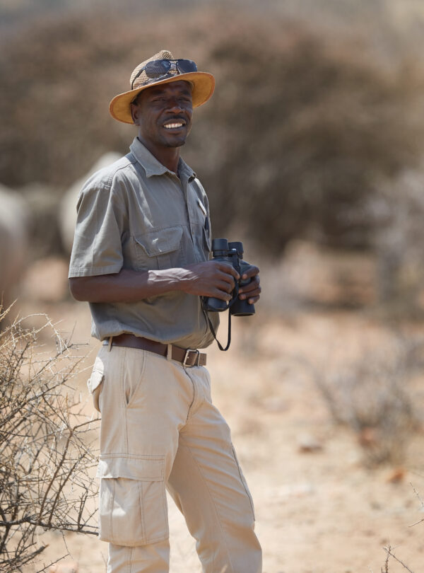 Portrait of a confident game ranger looking at a group of rhinos in the veld.