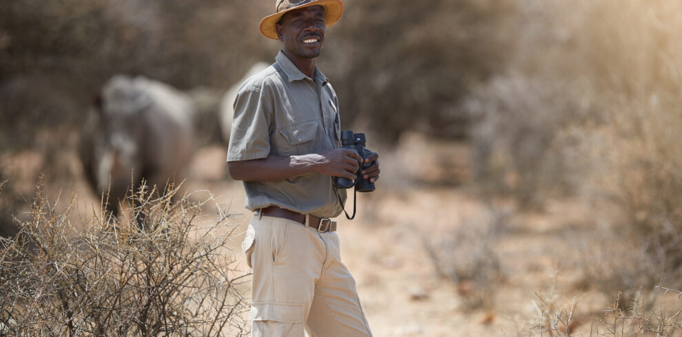 Portrait of a confident game ranger looking at a group of rhinos in the veld.